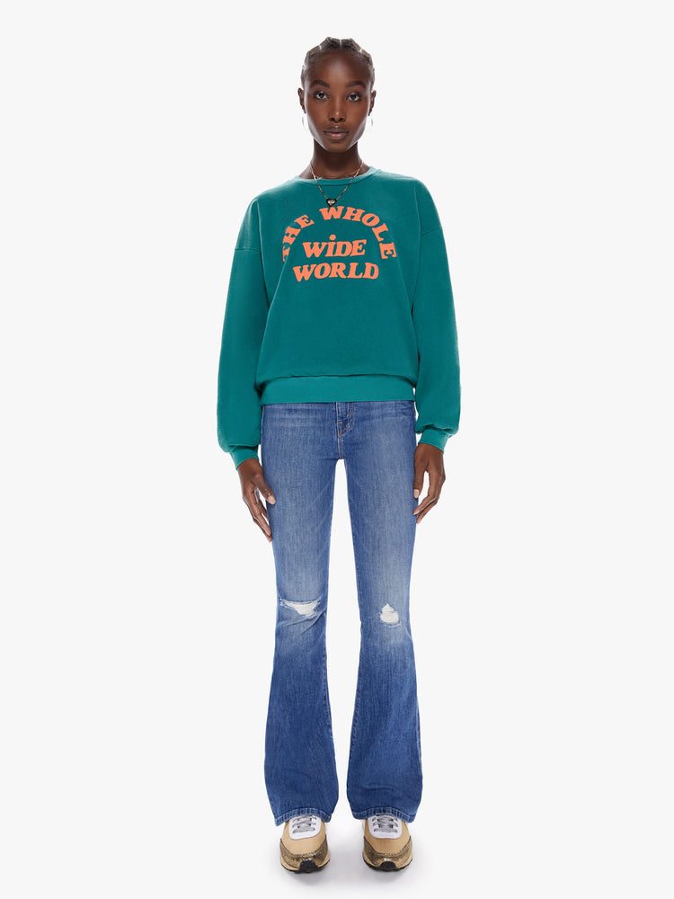 Full body view of a woman in a crewneck sweatshirt with dropped sleeves, a relaxed fit in a dark turquoise hue that features puff-ink text that reads The Whole Wide World