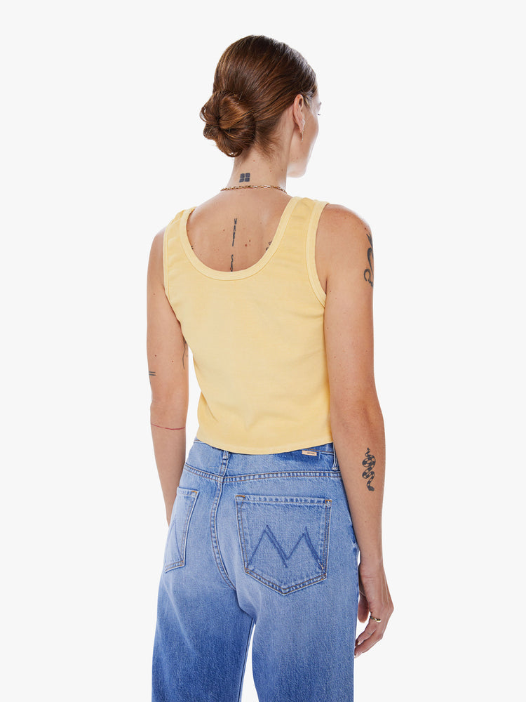 Back view of woman tank with a crewneck, thick straps and a cropped hem in a pastel yellow hue with green text.