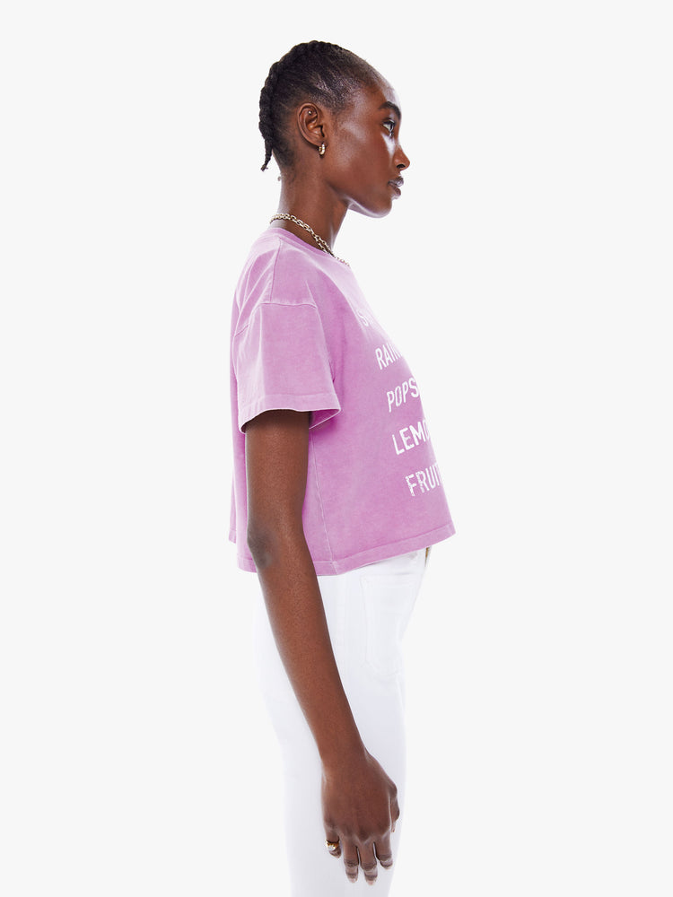 Side view of woman's cropped tee with a ribbed crewneck, drop shoulders and a boxy fit in a a washed fuchsia hue with white text.