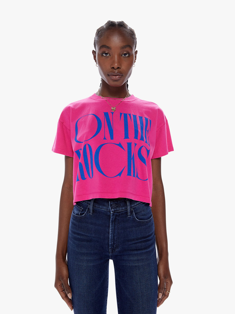 Front view of woman cropped tee with a ribbed crew neck, drop shoulders and a boxy fit in a bright fuchsia hue with blue text on the front.