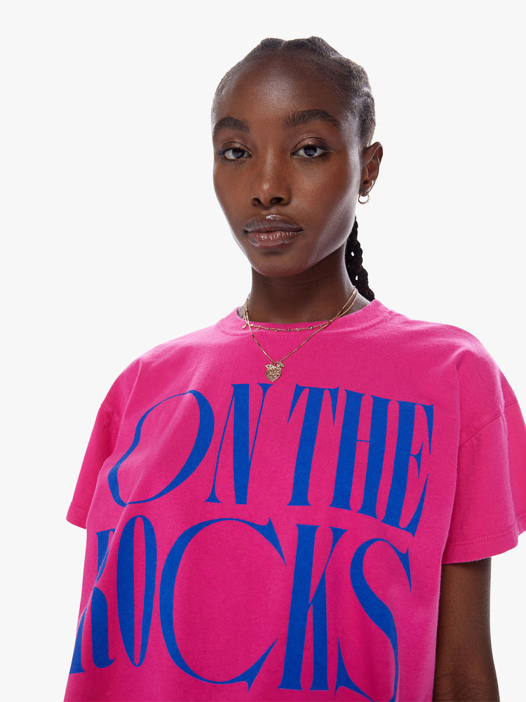 Close up view of woman cropped tee with a ribbed crew neck, drop shoulders and a boxy fit in a bright fuchsia hue with blue text on the front.