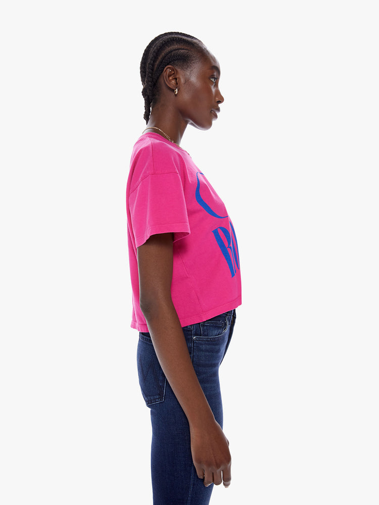 Side view of woman cropped tee with a ribbed crew neck, drop shoulders and a boxy fit in a bright fuchsia hue with blue text on the front.