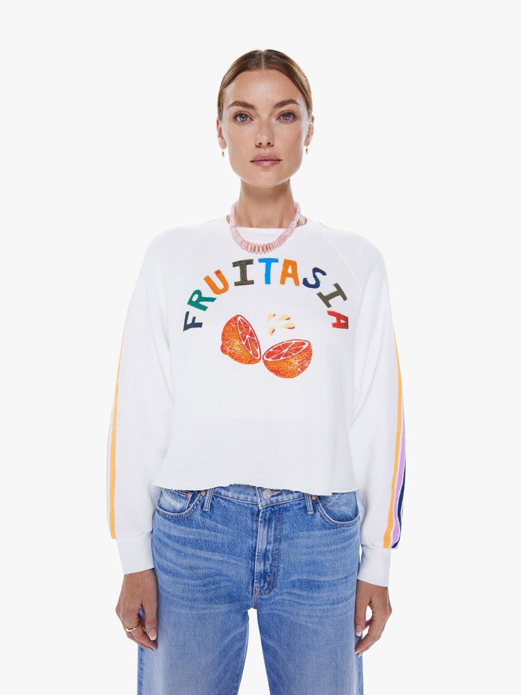 Front view of a woman cropped long sleeve tee with a crew neck, drop shoulders and a raw hem in white, with a colorful text graphic on the front and stripes down the sleeves.