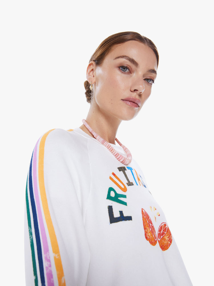 Close up side view of a woman cropped long sleeve tee with a crew neck, drop shoulders and a raw hem in white, with a colorful text graphic on the front and stripes down the sleeves.