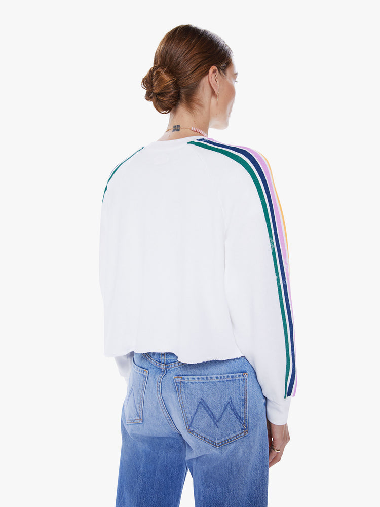 Back view of a woman cropped long sleeve tee with a crew neck, drop shoulders and a raw hem in white, with a colorful text graphic on the front and stripes down the sleeves.