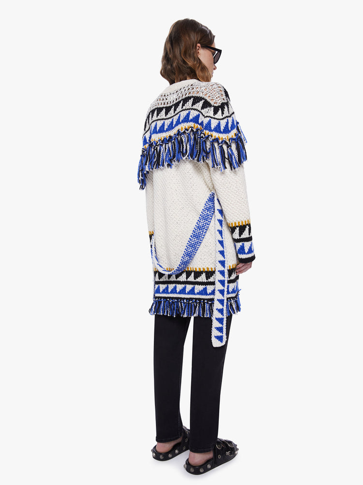 Back view of a womens black and blue triangle print thigh length cardigan sweater with orange knit details, tassels across the chest, arms, hems and a slight dropped shoulders and a boxy oversized fit