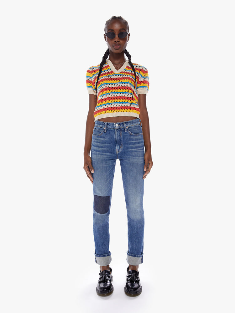 Full body view of a woman in a collared vneck blouse with short, slightly puffed sleeves and a cropped hem made from 100% cotton in bright orange, yellow and blue horizontal stripes, the knit top features a crochet style design with all over eyelets for a lightweight feel