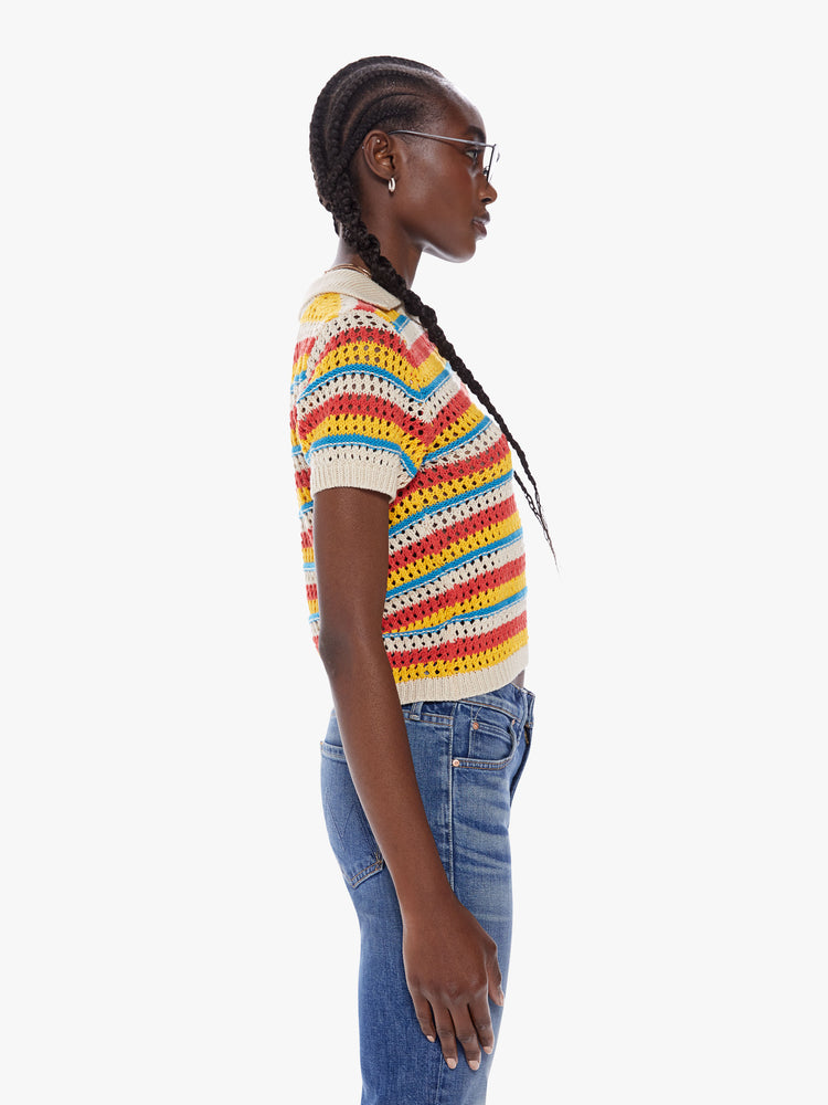Side view of a woman in a collared vneck blouse with short, slightly puffed sleeves and a cropped hem made from 100% cotton in bright orange, yellow and blue horizontal stripes, the knit top features a crochet style design with all over eyelets for a lightweight feel