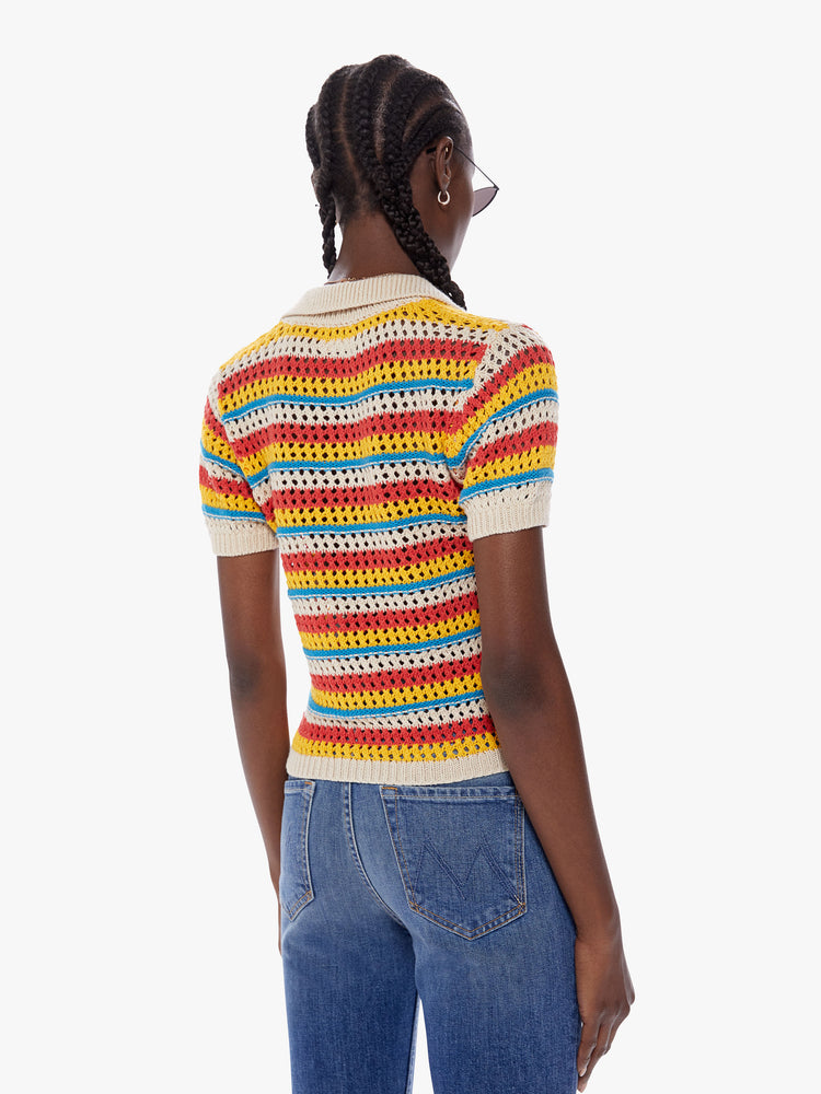 Back view of a woman in a collared vneck blouse with short, slightly puffed sleeves and a cropped hem made from 100% cotton in bright orange, yellow and blue horizontal stripes, the knit top features a crochet style design with all over eyelets for a lightweight feel