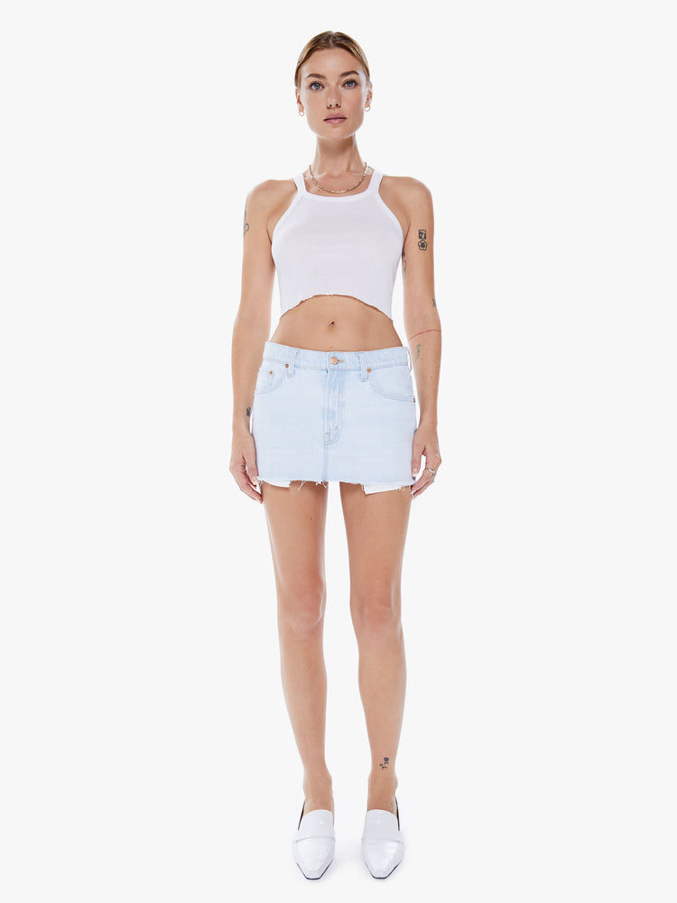 Woman denim mini skirt worn loose and low at the hips, the skirt features a zip fly, exposed pocket liners and a raw hem in a faded light blue wash.