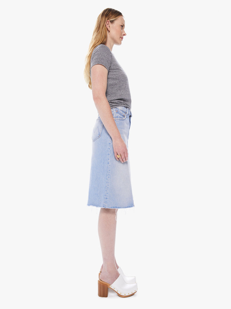 Side view of a women's light blue denim midi skirt with a front slit and a frayed hem
