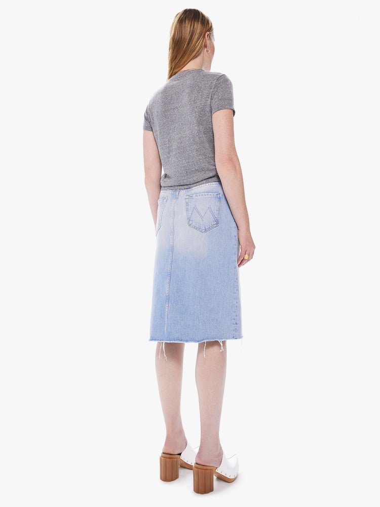 Back view of a women's light blue denim midi skirt with a front slit and a frayed hem