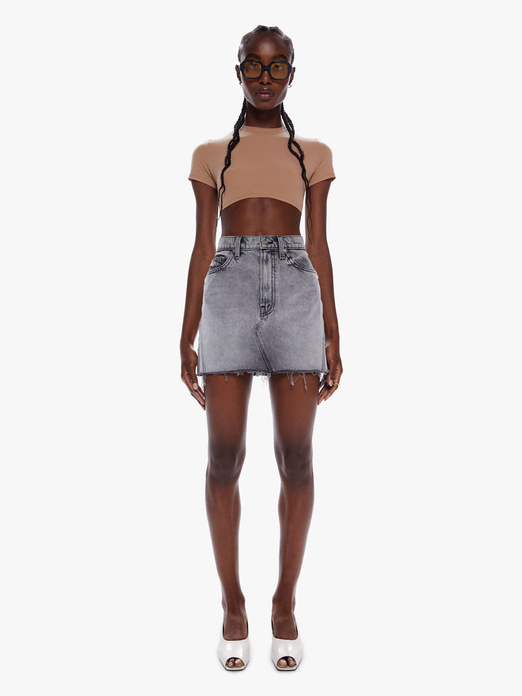 Front full body view of a woman in a denim mini skirt from snacks Mother homage to throwback styles of the 80s and 90s, this high rise denim skirt features a short frayed hem and a snug fit in a washed grey hue