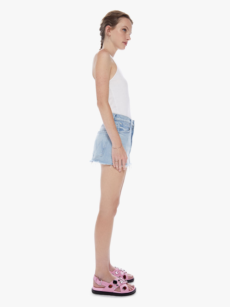 Side view of a woman denim mini skirt with a mid rise, frayed hem and exposed pocket lining in a light blue wash.