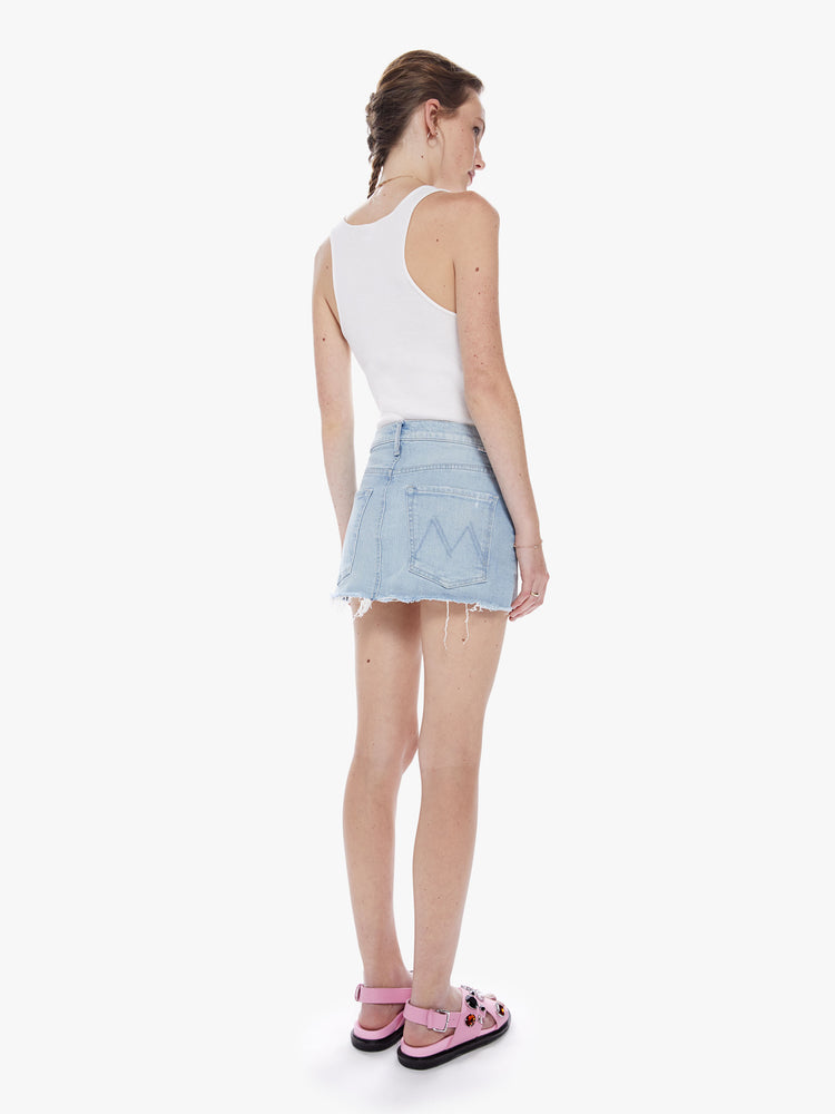 Back view of a woman denim mini skirt with a mid rise, frayed hem and exposed pocket lining in a light blue wash.