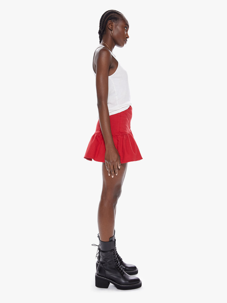 Side view of a womens red mini high rise skirt with a snug waist, side zipper, and ruffles along the hem.