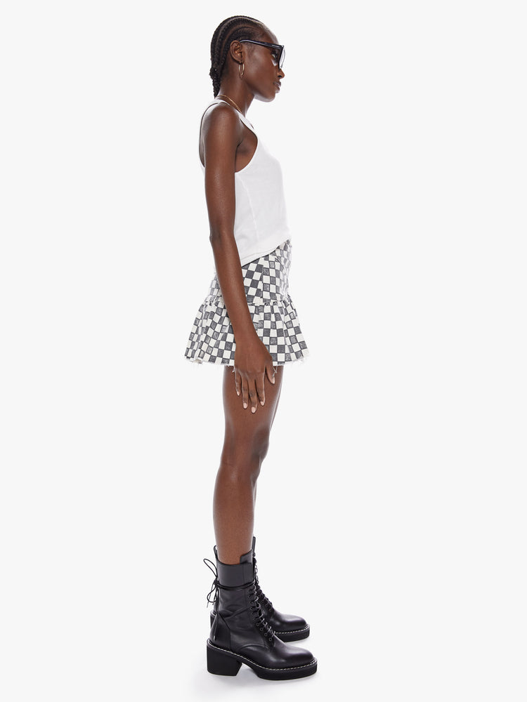 Side view of a womens black and white checkered mini high rise skirt with a snug waist, side zipper, and ruffles along the frayed hem.