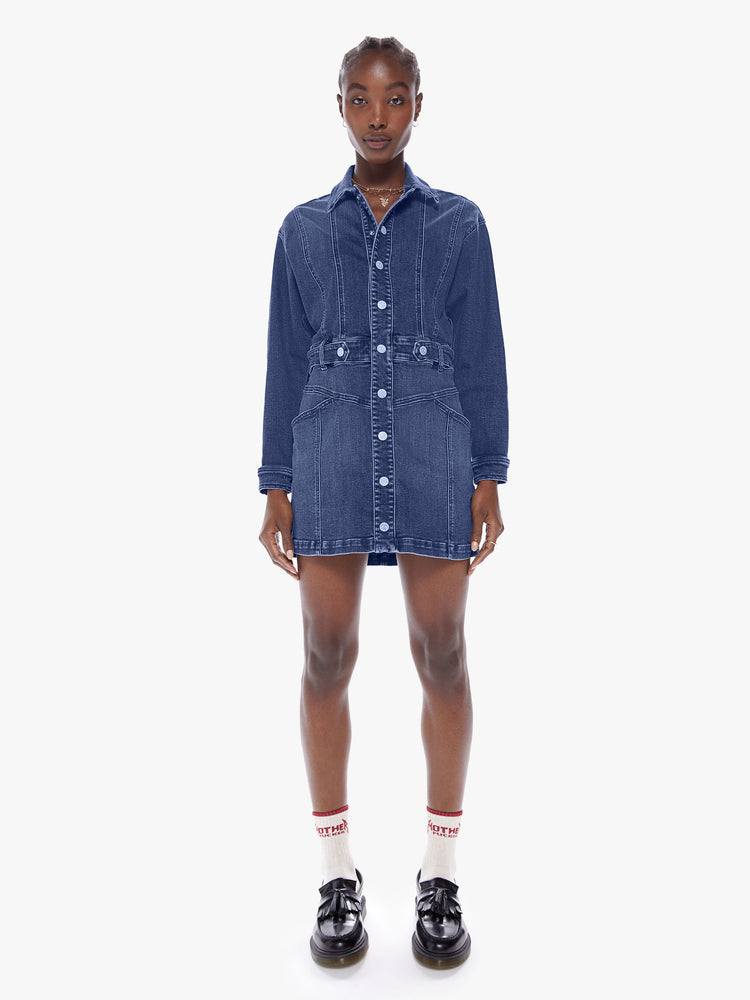 Front full body view of a woman in a collared denim mini dress with long batwing sleeves, a belted high waist and snaps down the front, cut from semi-rigid Superior denim in Beer Me that is a mid blue wash with fading, whiskering and a seamed details throughout
