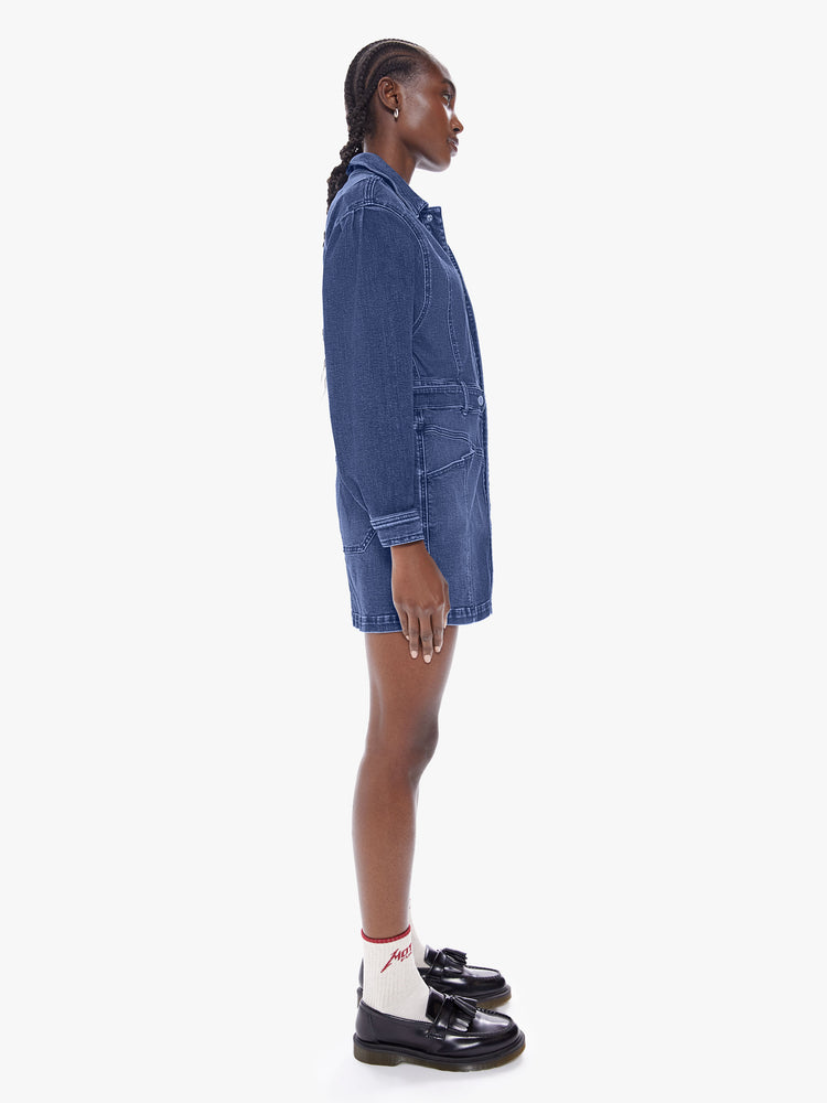Side full body view of a woman in a collared denim mini dress with long batwing sleeves, a belted high waist and snaps down the front, cut from semi-rigid Superior denim in Beer Me that is a mid blue wash with fading, whiskering and a seamed details throughout