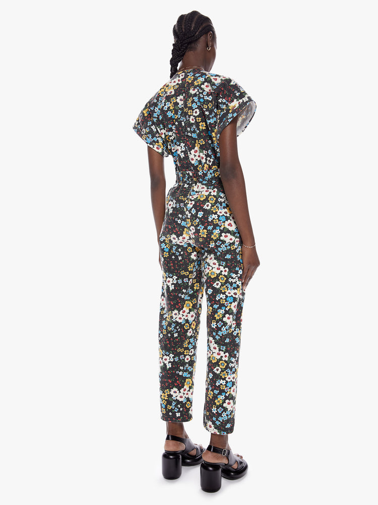 Back full body view a woman in a zip up jumpsuit featuring a vneck, rolled short sleeves, a cinched waist and a clean ankle length hem made from cotton with a touch of stretch, pushing daisies is a high contrast floral print in black, blue, yellow, red, and white