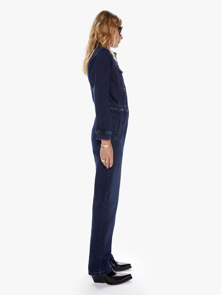 Side view of womens mechanic inspired zip up dark blue denim wash jumpsuit with collared neck, patch pockets, high rise elastic waistband and long sleeves.