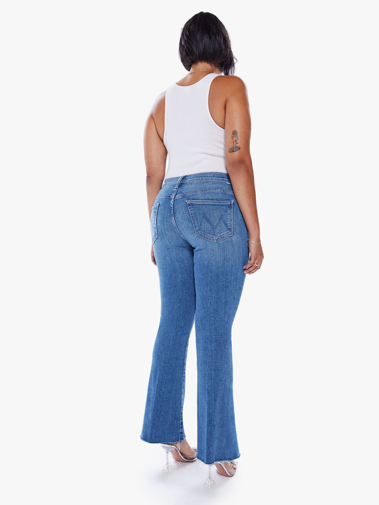 Back view of a womens medium blue wash denim jean featuring a flare leg with a frayed hem.