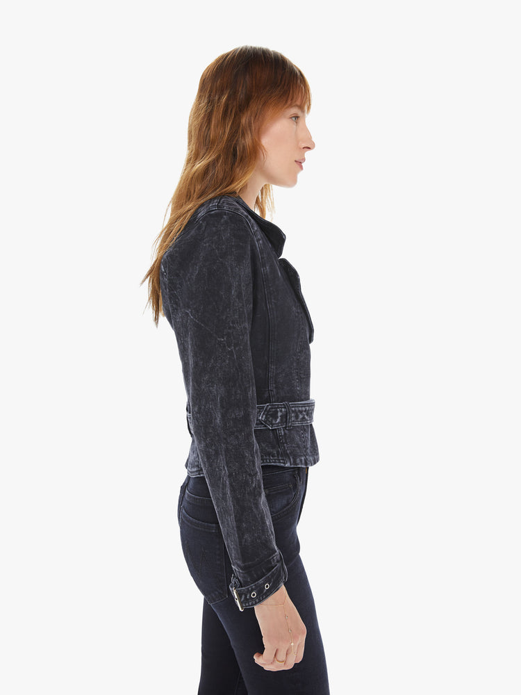 Side view of a woman wearing a washed black moto jacket featuring a fitted, cropped body and a belted waist.
