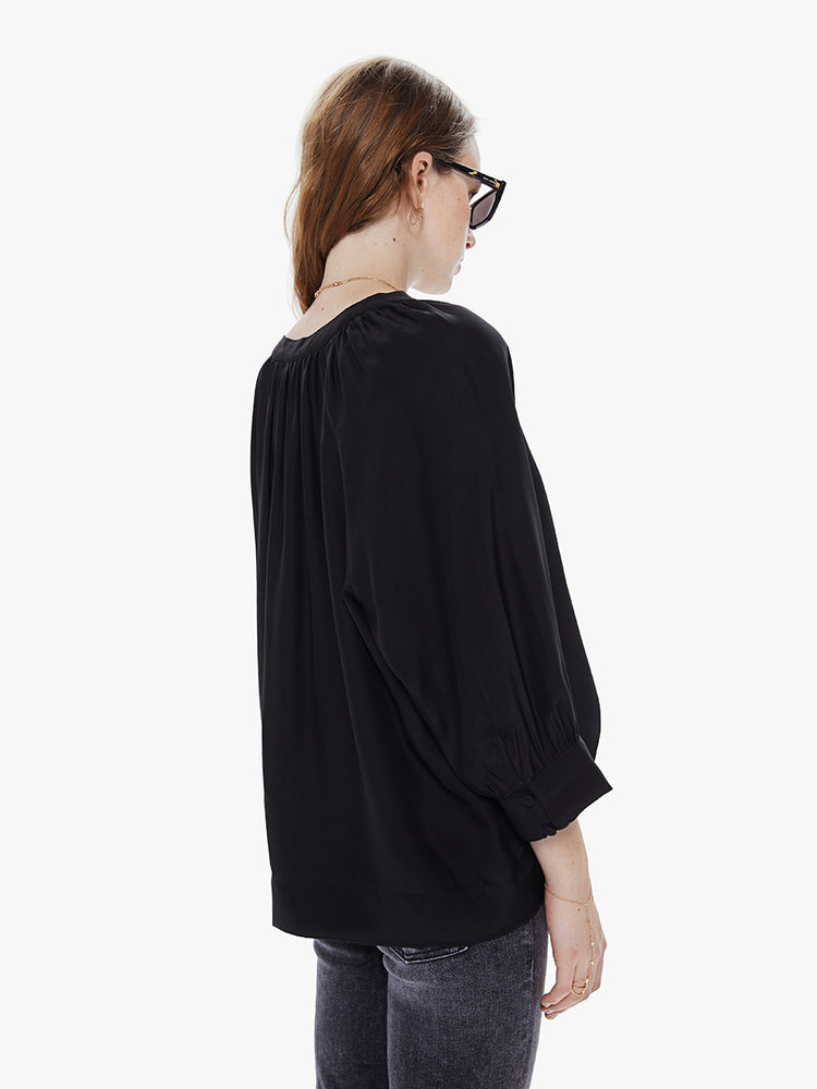 A back view of a Womens black blouse featuring a v-shaped neckline, covered buttons, and subtle pleats below the collar.