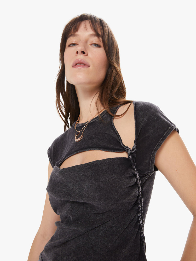 A closeup detail view of a Womens asymmetrical sleeve top in a black mineral wash, featuring cutouts at the shoulder and chest and a braid down the left side.