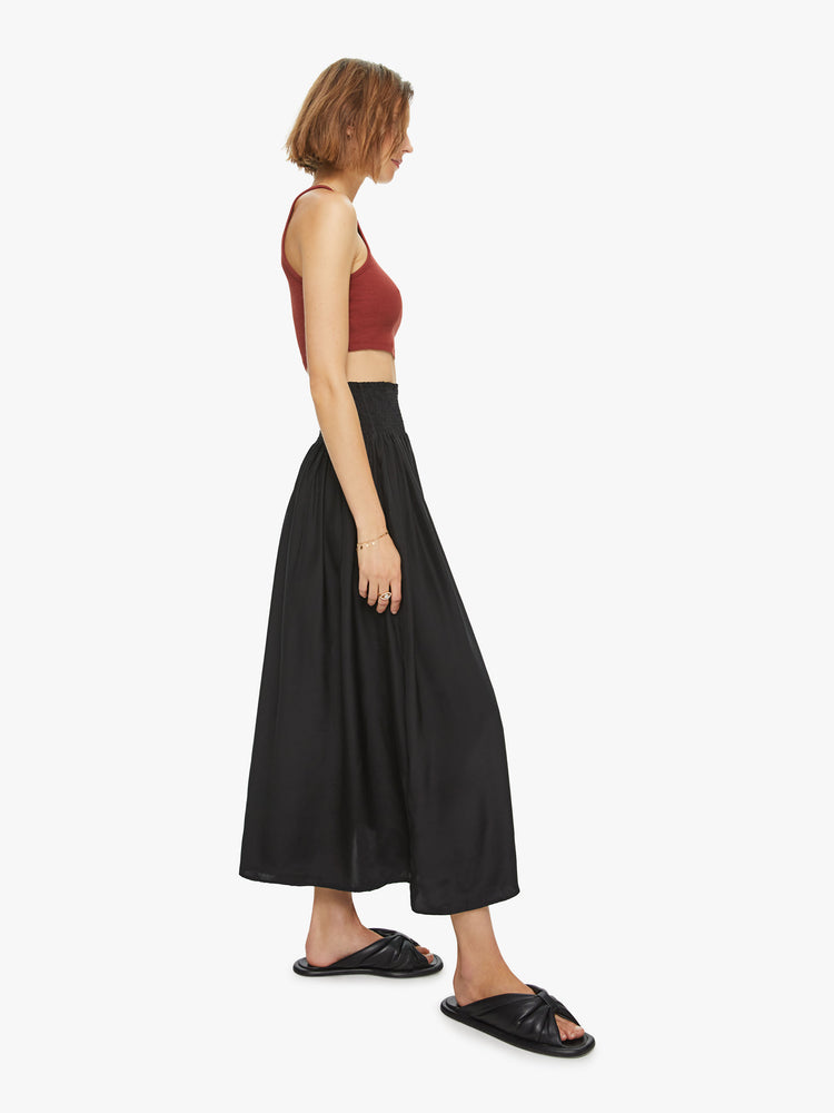Side view of a womens black mid length skirt, featuring an elastic high rise waist and flowy fit.