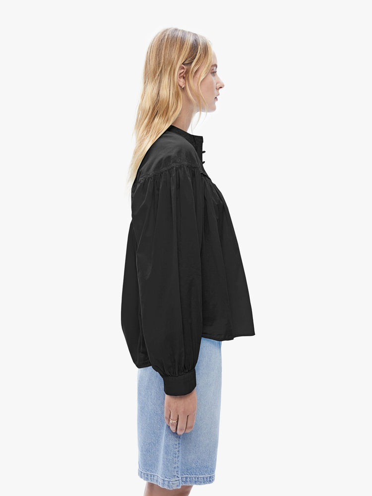 Side view of a woman in XiRENA loose, flowy top that has a buttoned v-neck, long balloon sleeves and ruffles throughout for a voluminous fit in black.