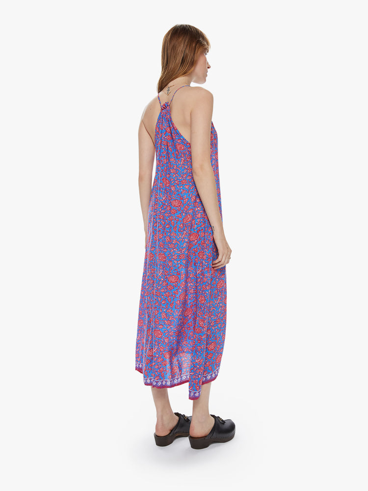 Back view of a woman wearing a maxi dress featuring a halter neck with white tassels and a blue and pink floral print.