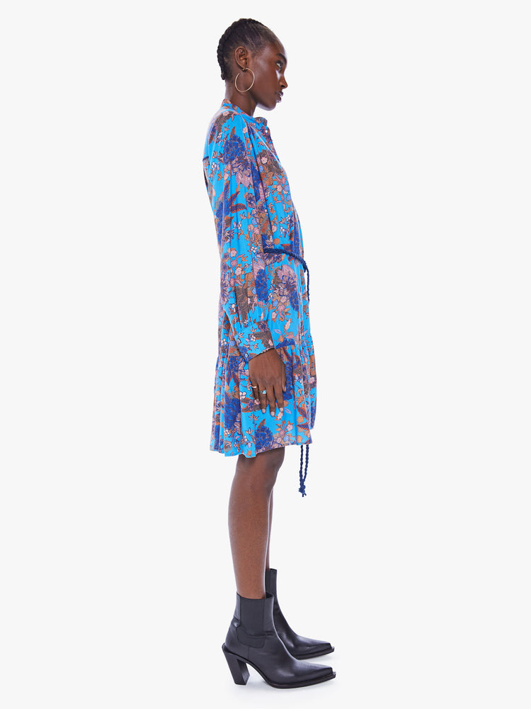 Side view of a womens blue floral print button down dress featuring long sleeves and a blue rope belt.