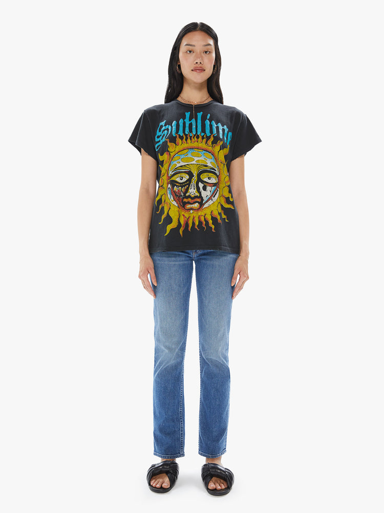 Front full body view of a woman wearing a faded black crew neck tee featuring a large "Sublime" sun graphic.