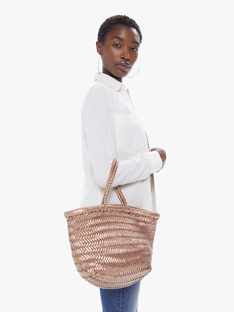 Side view of a woman holding a metallic brown, woven leather bag.