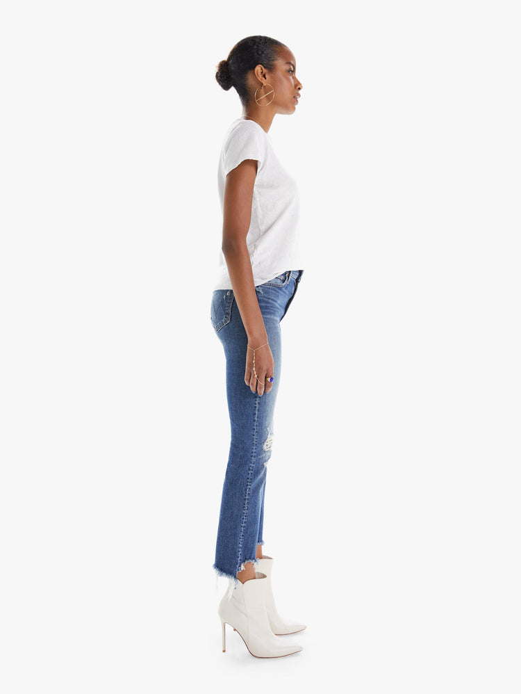 side view of women's medium blue boot cut jean with a high rise, distressing, and chewed hems