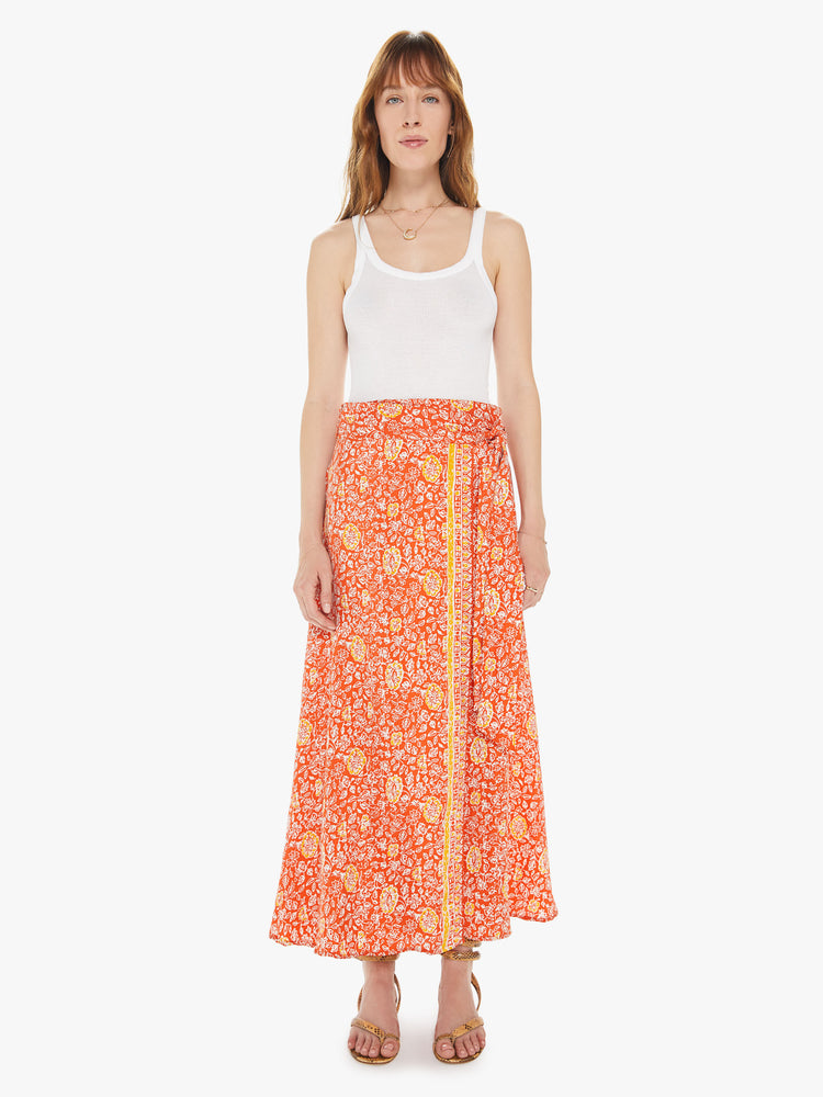Front view of a woman wearing a bright orange maxi skirt featuring a yellow print, a high waist, and a side wrap tie.