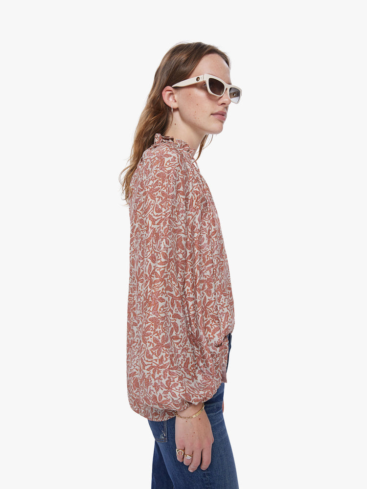 A side view of a woman wearing a delicate orange and cream floral print long sleeve blouse with collar