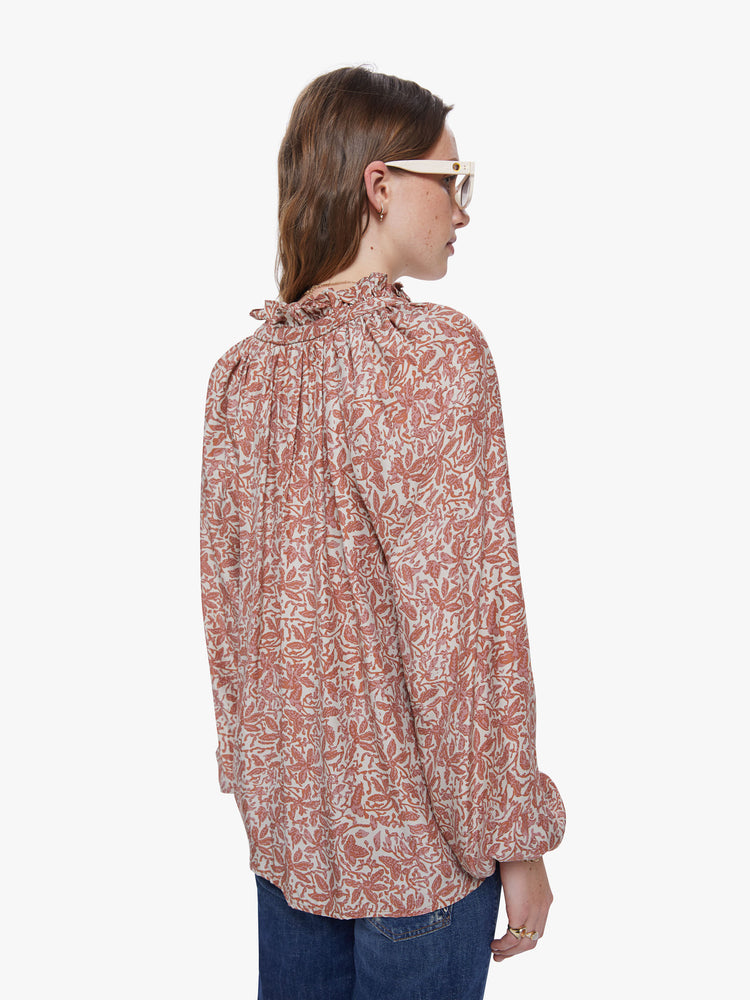 A back view of a woman wearing a delicate orange and cream floral print long sleeve blouse with collar