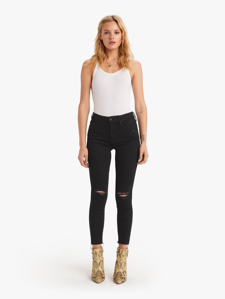 front view of women's black mid rise skinny jean with distressed knees, zip fly, ankle inseam, and frayed hem