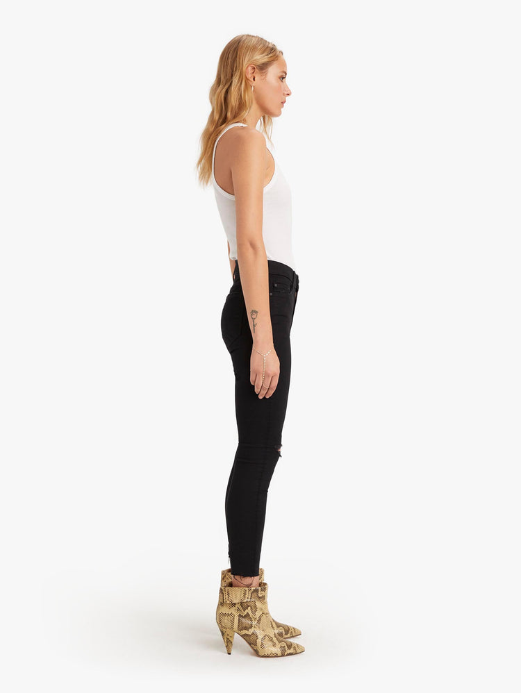 side view of women's black mid rise skinny jean with distressed knees, zip fly, ankle inseam, and frayed hem