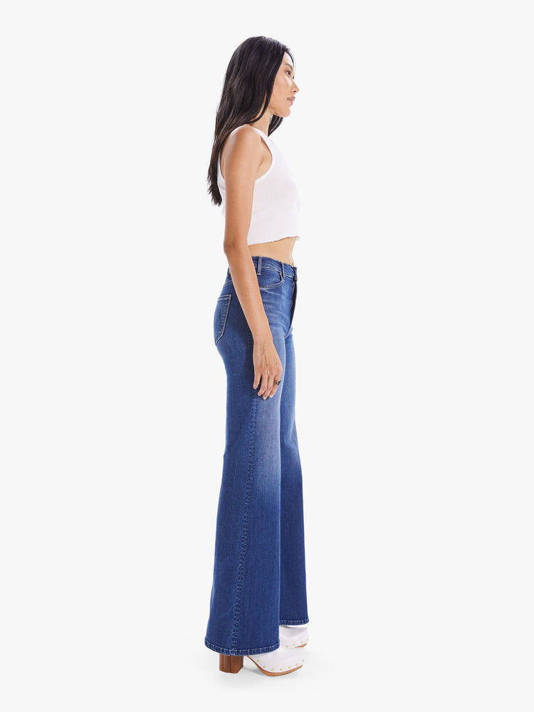 Side view of a woman wearing high rise, wide leg jeans in a medium blue wash denim with light fading and whiskering.