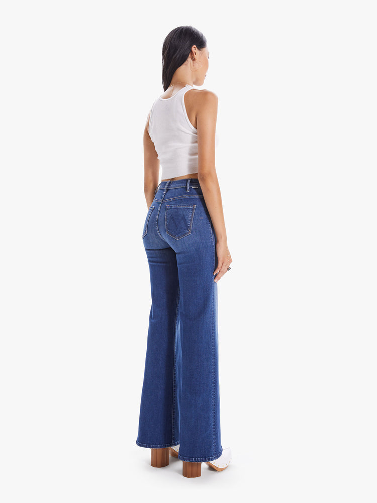 Back view of a woman wearing high rise, wide leg jeans in a medium blue wash denim with light fading and whiskering.