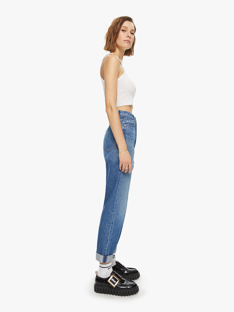 Side view of a womens medium blue wash jean featuring a high rise, relaxed straight leg, and a cuffed hem.