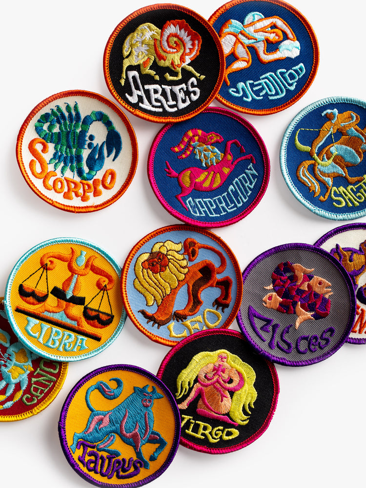 A top front view of scattered, round embroidered patches each featuring the different astrological zodiac signs.