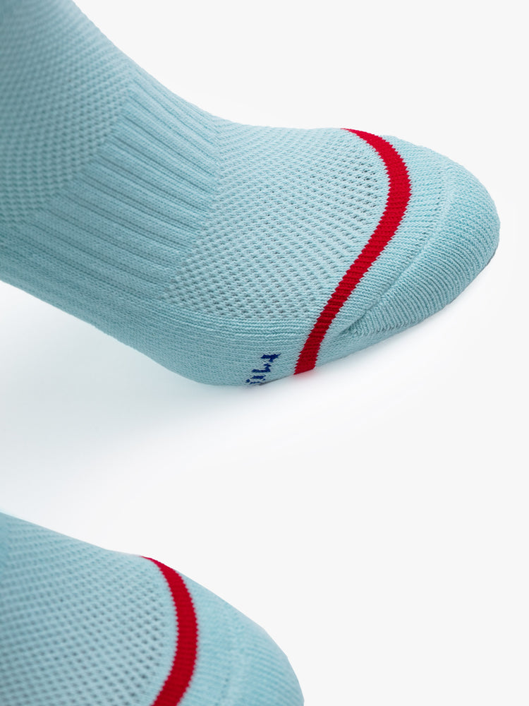 Close up view of a pair of light blue socks featuring a red stripe and "OUI" in navy blue.