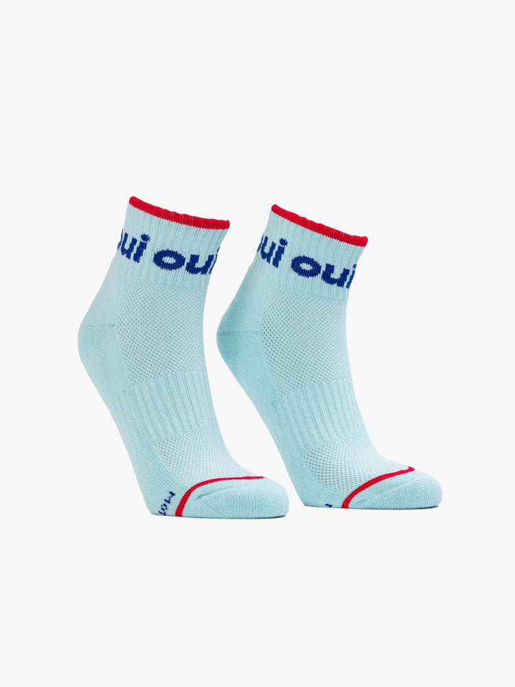 Front view of a pair of light blue socks featuring a red stripe and "OUI" in navy blue.