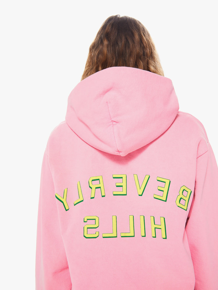 Womens back body close up view of a bright pink pullover hoodie sweatshirt with a slightly oversized fit featuring a yellow puff print reading "BEVERLY HILLS" in reverse