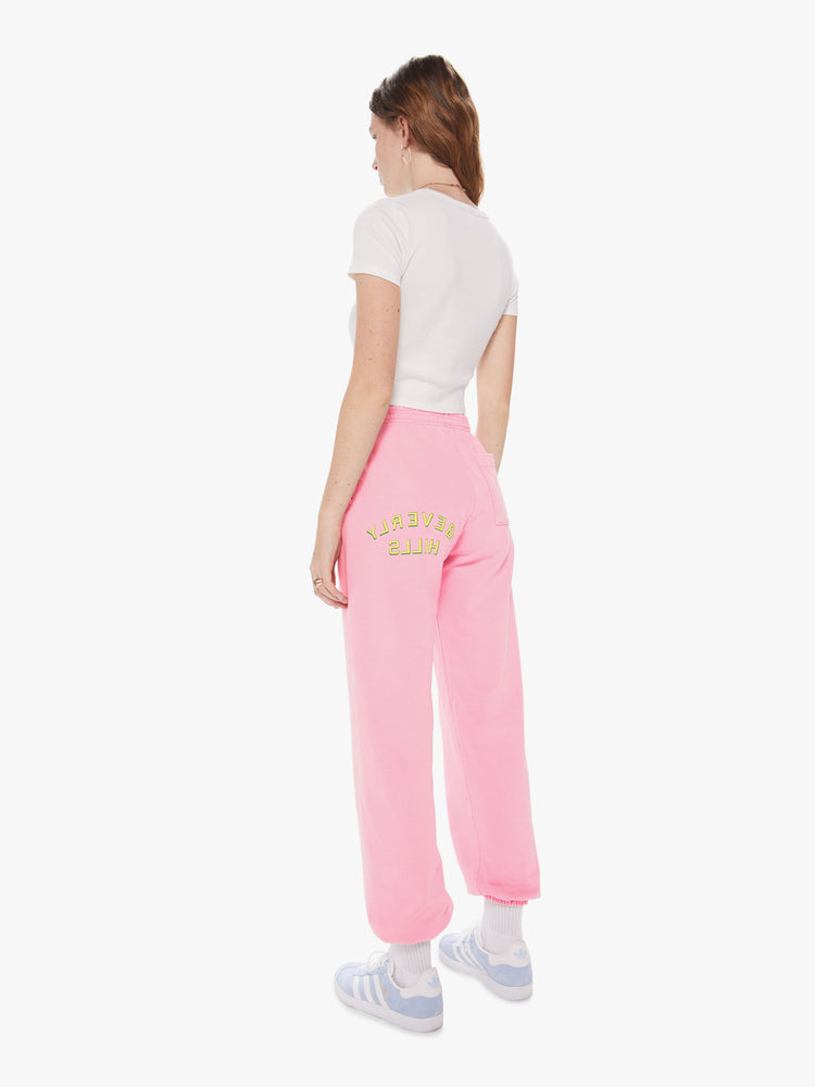 Womens back 3/4 full body view of a pair of bright pink sweatpants with a slightly oversized fit and elastic waist and cuffs, featuring a yellow puff print on the back left thigh reading "BEVERLY HILLS"