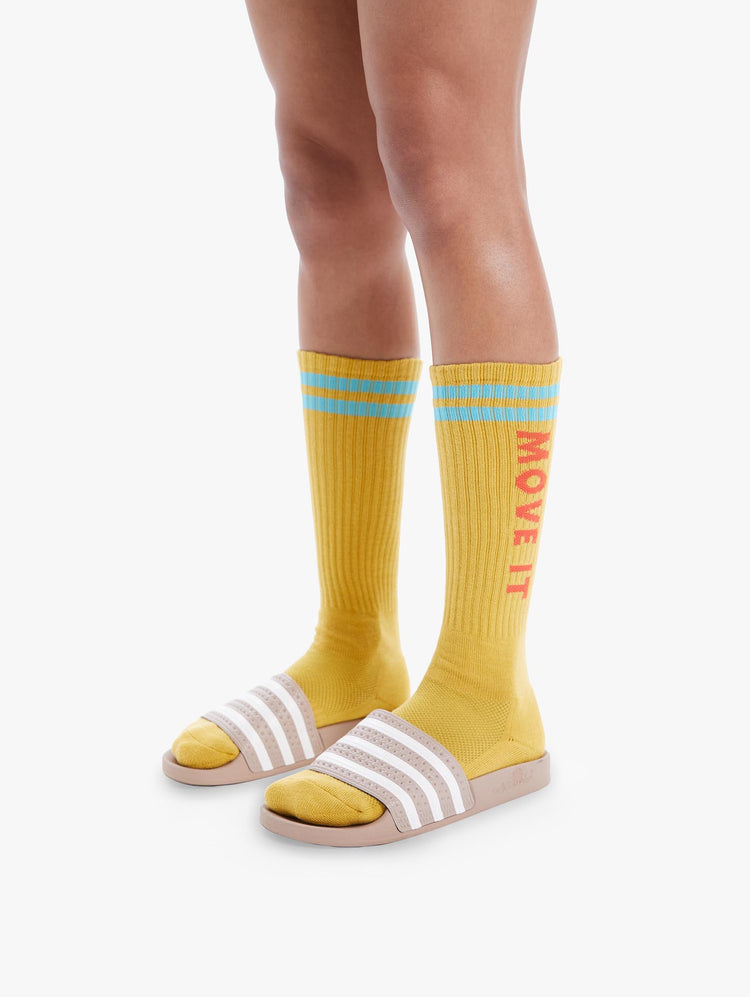 SIDE VIEW WOMEN'S YELLOW TALL SOCK WITH LIGHT BLUE STRIPING AT THE TOP ORANGE MOVE IT SIDE LETTERING AND BLACK BOTTOM LETTERING